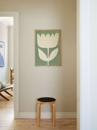 Stampa floreale verde e crema con cornice in legno sopra uno sgabello chiaro in un corridoio beige