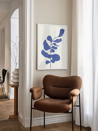 Framed abstract blue botanical print above a brown armchair in a bright corner