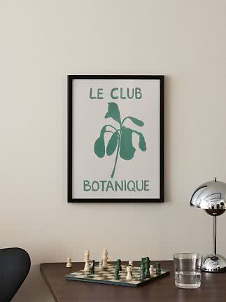 Poster incorniciato con pianta verde e scritta "Le Club Botanique" sulla parete sopra un tavolo