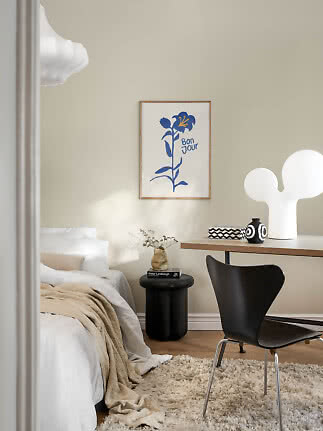 Cozy bedroom with desk, black chair, white table lamp, and floral poster on a beige wall