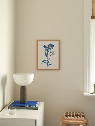 Framed print with blue flower and the text "Bon Jour" on a beige wall