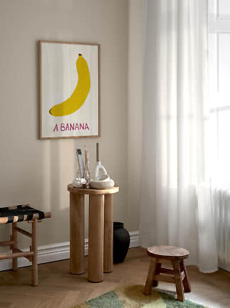 Inramad poster med gul banan på beige vägg i ett ljust rum