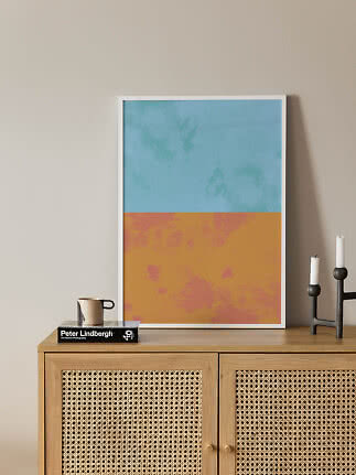 Abstrakt plakat i hvid ramme med blå top og orange bund, lænet på træskænk