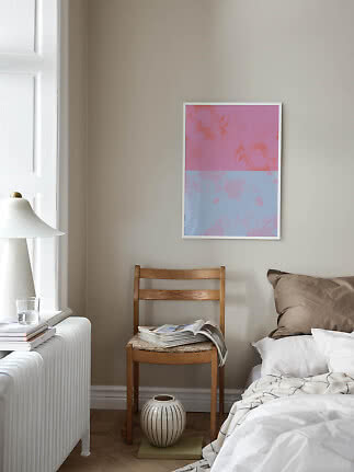 Poster astratto incorniciato rosa e azzurro sopra una sedia accanto al letto in una camera luminosa