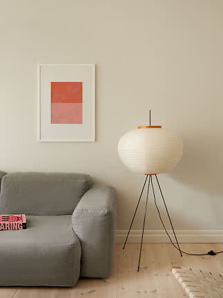 Hvid gulvlampe med papirskærm ved siden af en grå sofa i en minimalistisk stue