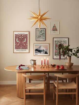 Sala da pranzo accogliente con tavolo in legno, sedie, lampada a stella, stampe e candele rosse