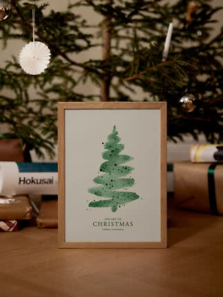 Gerahmter Weihnachtsdruck mit grünem Aquarellbaum auf Tisch vor geschmücktem Baum