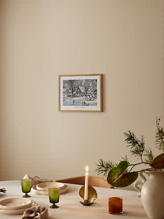 Indrammet vintermotiv på beige væg over dækket bord med lysestage, glas og vase med grene