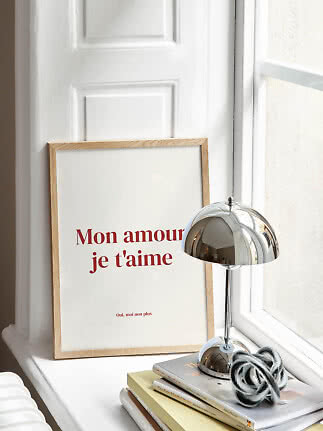 Indrammet plakat med teksten "Mon amour je t'aime" ved siden af en kromlampe på en vindueskarm