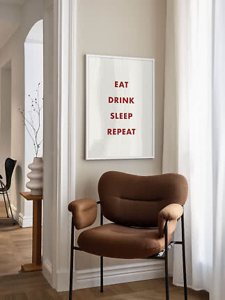 Indrammet plakat med rød tekst over en brun lænestol ved lyse gardiner