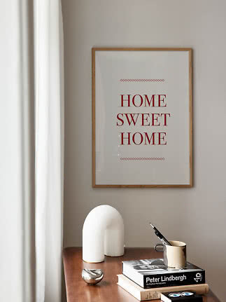 Poster incorniciato "Home Sweet Home" sopra un tavolo in legno con libri e oggetti decorativi