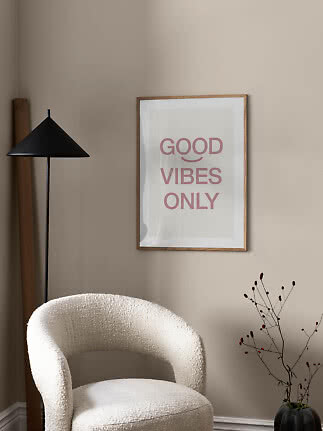 Poster incorniciato con scritta "GOOD VIBES ONLY" su parete beige sopra poltrona bianca