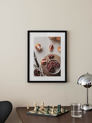 Affiche de fruits encadrée en noir au-dessus d’une table avec échiquier, verre et lampe chromée