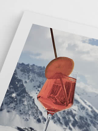 Pink drink in a wine glass with orange slice and straw in front of a snowy mountain photo