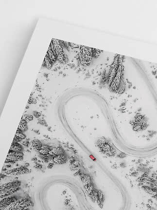 Indrammet luftfoto af snoet vintervej i sneklædt skov med en rød bil