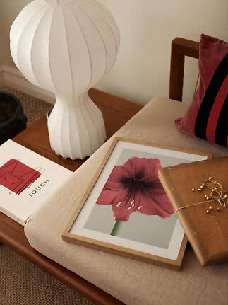 Lámpara de mesa escultural blanca sobre mesa de madera junto a sillón beige con flor enmarcada