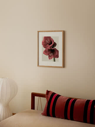 Lámina floral con marco de madera y flores rojo oscuro en pared beige sobre la cama