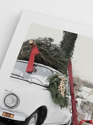 Foto incorniciata di un’auto d’epoca bianca con albero di Natale sul tetto e rami con campanelli dorati