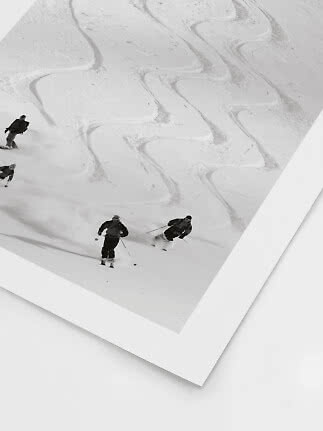 Zwart-witfoto van skiërs op een steile besneeuwde helling met slingerende sporen in de sneeuw