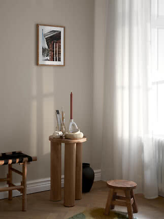 Lyst hjørne med lille træskammel, rundt sidebord og indrammet foto på beige væg