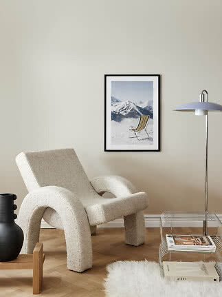 Moderne stue med cremefarvet lænestol, gulvlampe og indrammet bjergplakat på væggen