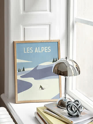 Indrammet Les Alpes-skiposter på vindueskarm ved siden af krombordlampe og bøger