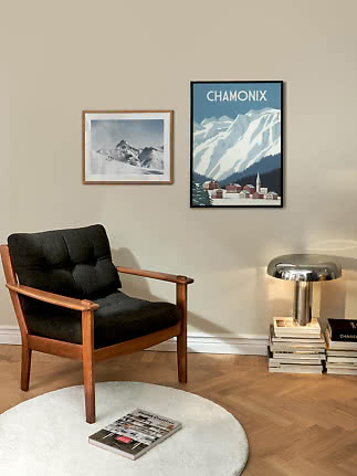 Hyggeligt hjørne med sort lænestol, lampe og Chamonix-plakat på beige væg