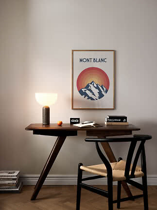 Skrivebord i mørkt træ med stol, bordlampe, bøger og Mont Blanc-plakat på væggen