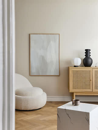 Minimalistisk stue med cremefarvet lænestol, abstrakt maleri og lyst træskab med lamper og vase