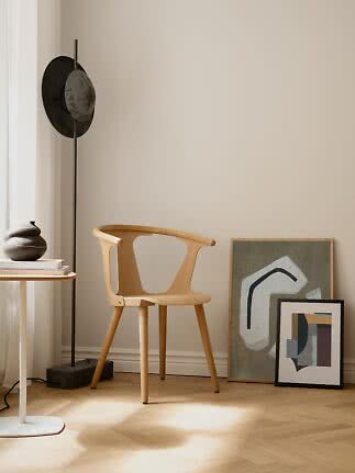 Light wood chair in a minimalist corner with black floor lamp and framed abstract art