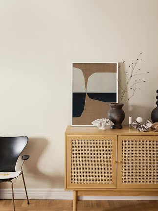 Light wood cabinet with cane doors, abstract print, dark vase and decor against a beige wall