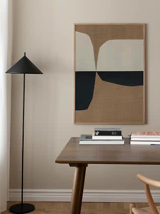 Abstract framed wall art above a wooden table with books and a black floor lamp