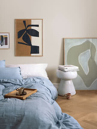 Chambre avec linge de lit bleu clair, plateau en bois avec tasse et art abstrait au mur.