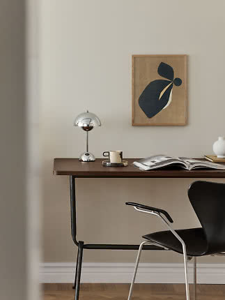 Scrivania con lampada cromata, tazza, libro aperto e quadro astratto in una stanza minimalista