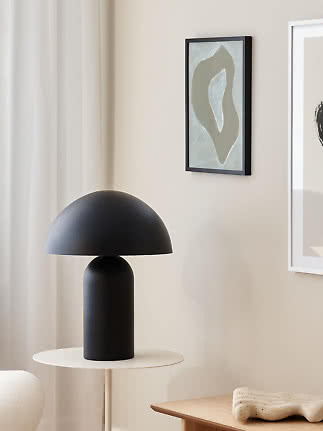 Lámpara de mesa negra con pantalla de cúpula sobre mesa auxiliar blanca en una estancia moderna