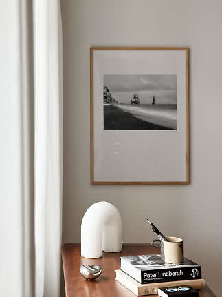 Framed black-and-white coastal photo on beige wall above wooden table with books, mug and white sculpture
