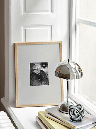 Lampe de table chromée sur rebord de fenêtre avec livres et cadre photo fleur en noir et blanc