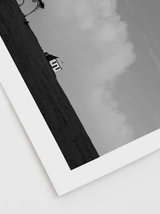 Schwarz-Weiß-Foto eines kleinen Hauses an einem schrägen Hang unter dramatischen Wolken