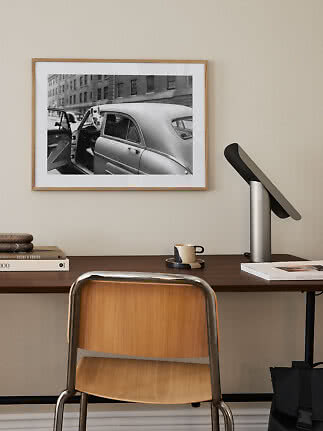 Skrivebord med træstol, sort bordlampe og indrammet sort-hvid fotoprint på væggen