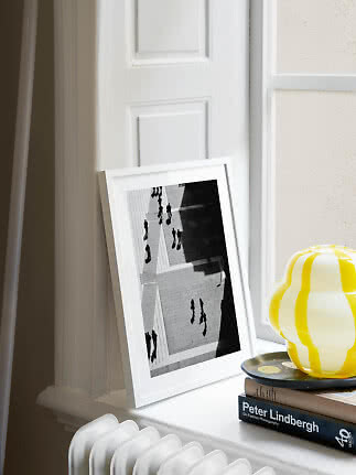 White framed black-and-white print leaning on a windowsill beside a yellow striped lamp