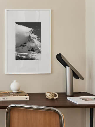 Schwarz-weißes Bergposter im weißen Rahmen über dunklem Schreibtisch mit Lampe, Büchern und Vase