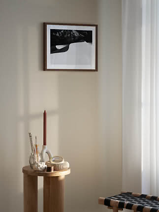 Framed black-and-white landscape print on a beige wall above a small wooden side table