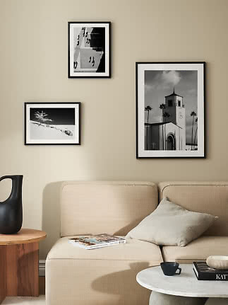 Três fotografias em preto e branco emolduradas sobre um sofá bege numa sala moderna.