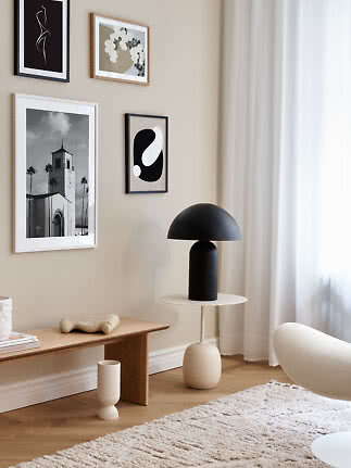 Sala moderna com parede bege, quadros, luminária preta, banco de madeira e cortinas leves