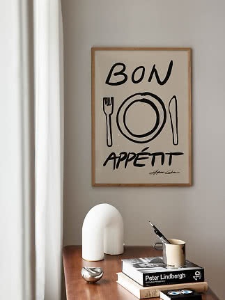 Indrammet Bon Appétit-plakat med tallerken, gaffel og kniv på beige væg over træbord