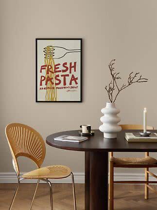 Affiche Fresh Pasta encadrée au-dessus d'une table avec vase blanc, bougie et chaises en bois