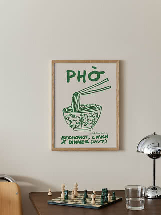 Indrammet plakat med grøn pho-illustration og tekst på en lys væg over et bord med skakbræt.