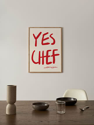 Indrammet plakat med rød håndskrift "YES CHEF" over et spisebord.