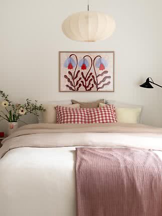 Chambre lumineuse avec lit beige, plaid rose, coussin à carreaux et tableau floral