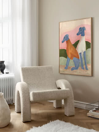 Indrammet farverigt maleri med to stiliserede hunde på beige væg over en lys lænestol.